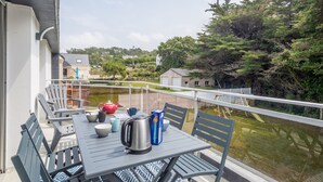 Un balcon avec une table dressée pour deux personnes, donnant sur une étendue d’eau et une zone boisée.