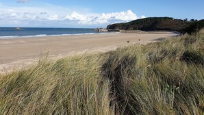 Une plage bordée de dunes herbeuses, avec une falaise rocheuse en arrière-plan.