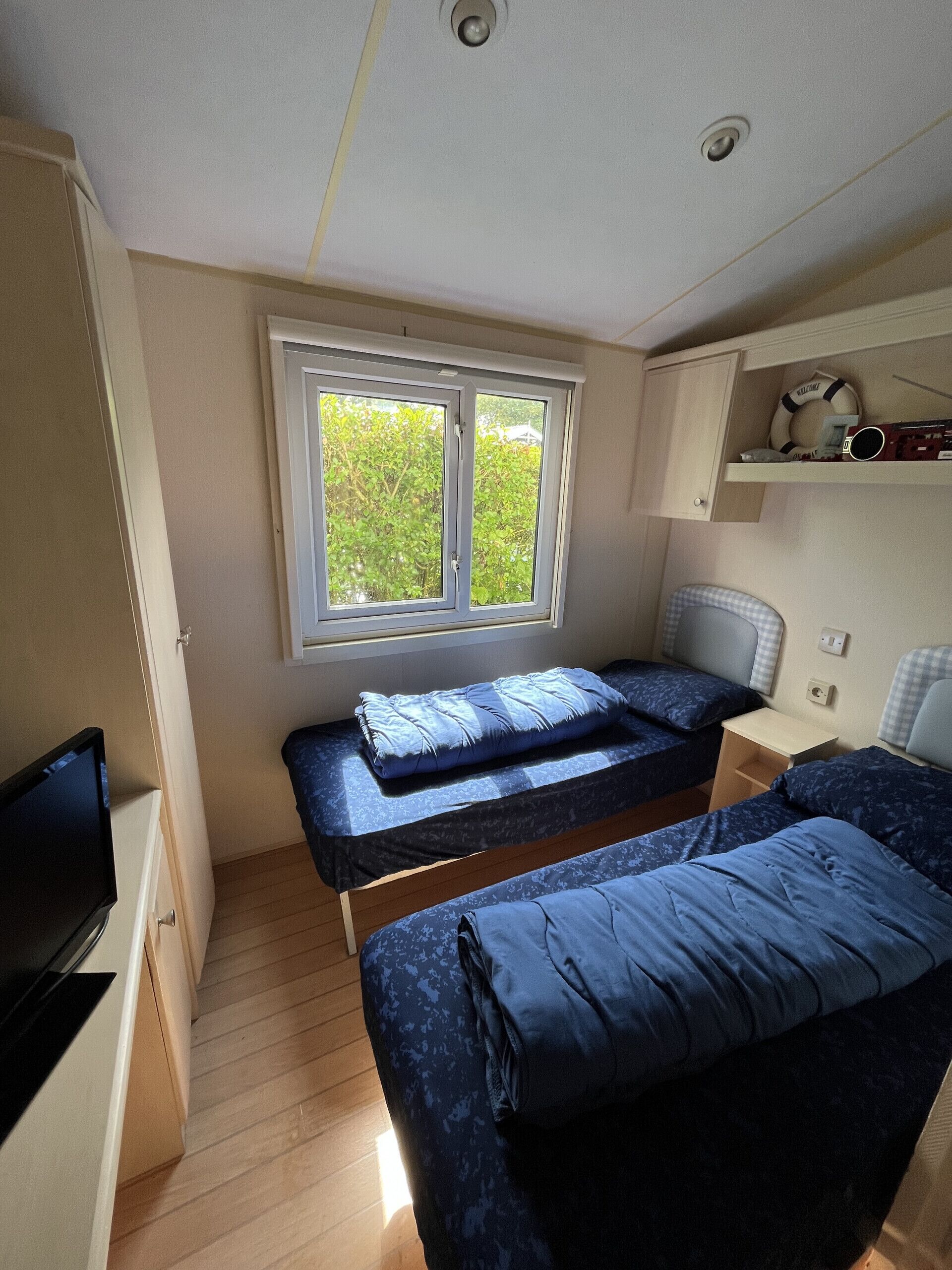 A compact room with two beds, a television, and a window with a view of greenery.