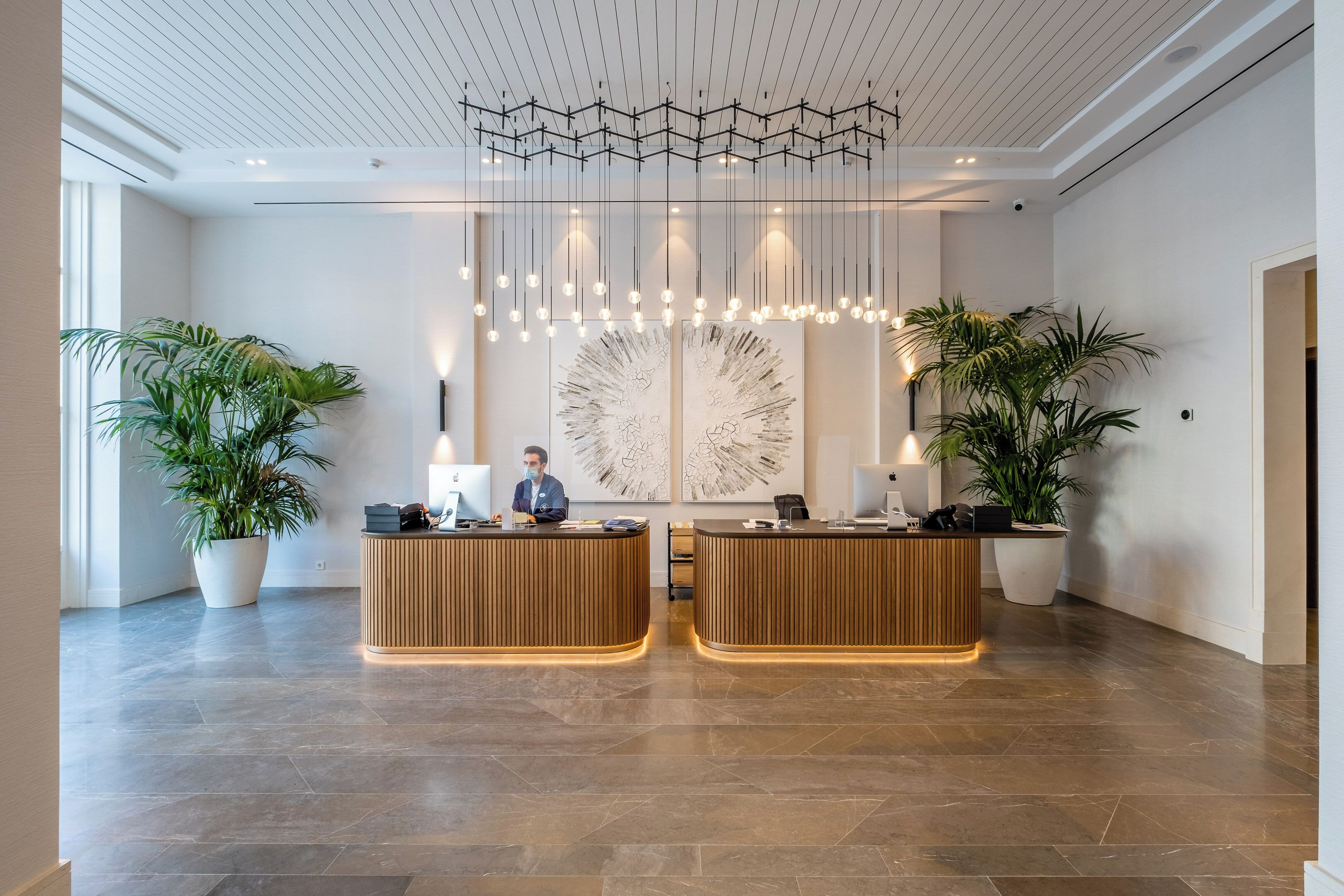A modern reception area with two wooden reception desks, a large abstract painting on the wall, and hanging pendant lights.