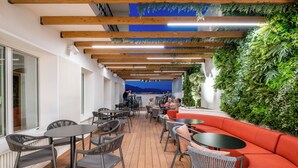 An outdoor seating area with tables and chairs, a red sofa, and a green wall with plants. - Soho Boutique Equitativa (Málaga)