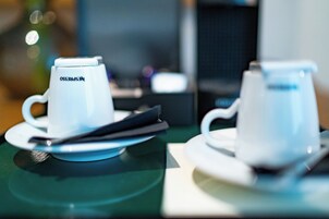 Two white coffee cups with lids on saucers, placed on a table with a blurred background.