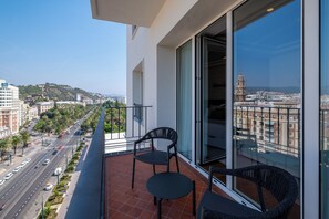 A balcony with two chairs and a table, overlooking a city street with palm trees and buildings. - Petit Palace La Equitativa formerly known as Soho Boutique Equitativa (Málaga)