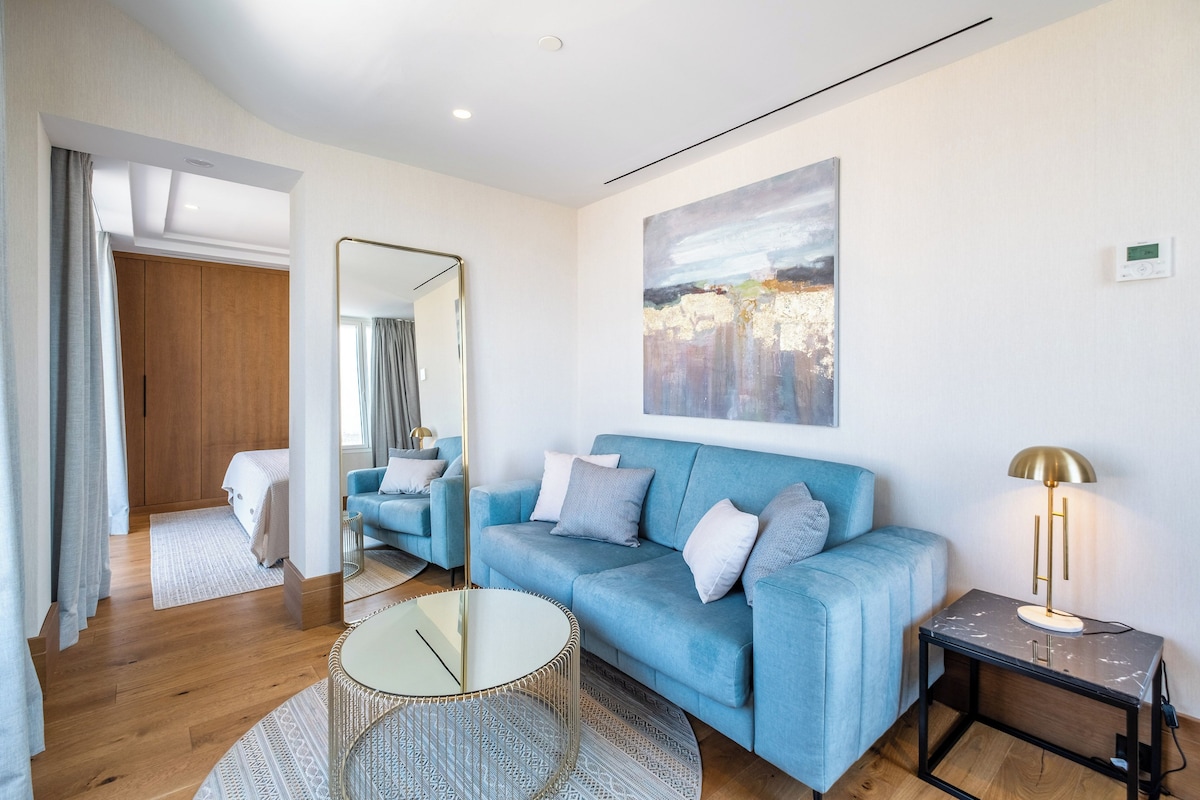 A modern living room with a blue sofa, a round coffee table, a floor lamp, and a large abstract painting on the wall.