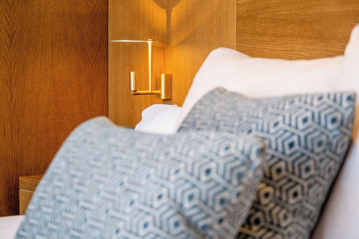 A hotel room with a wooden headboard, a bedside table, and patterned pillows.