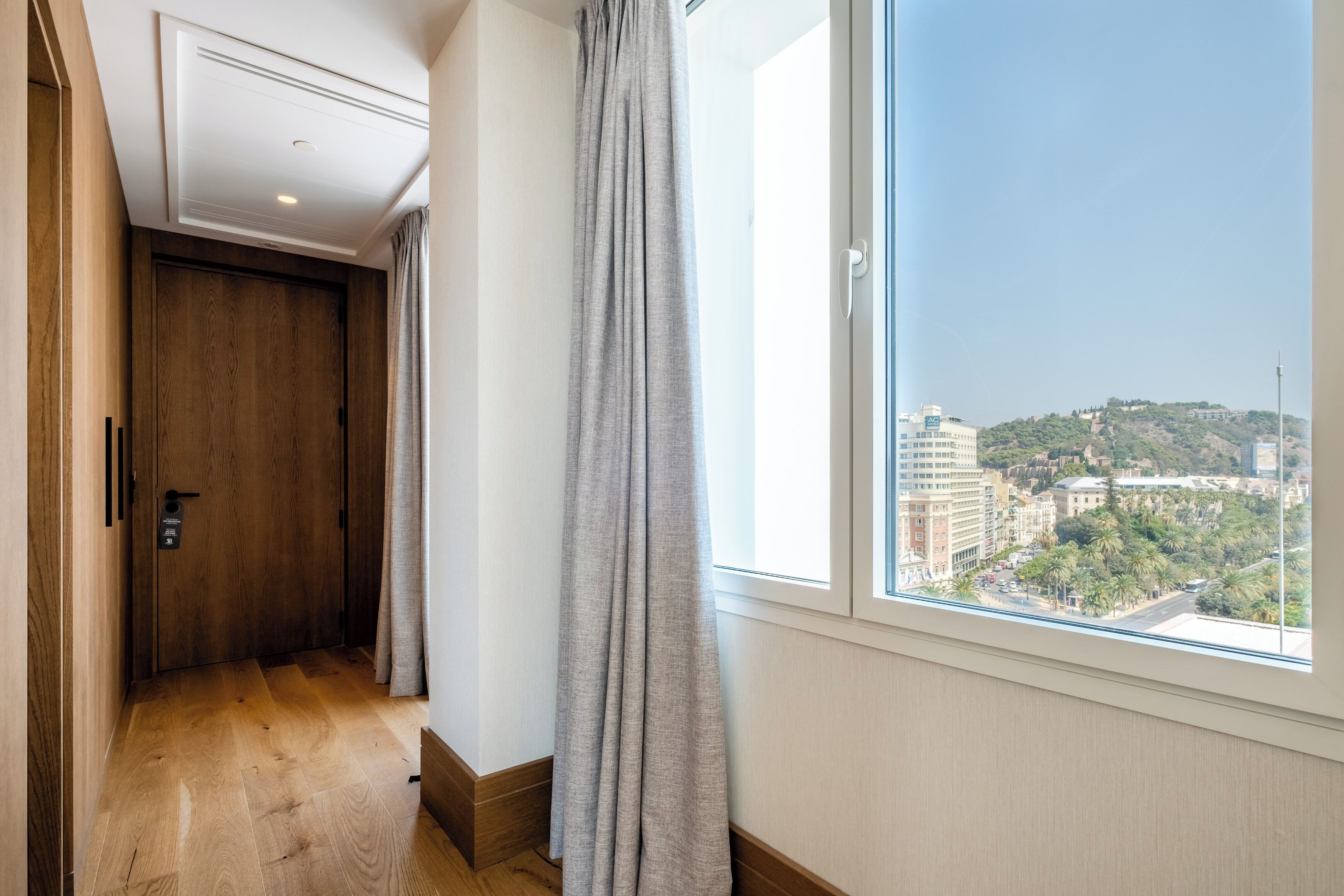 Un pasillo con una puerta de madera, una ventana que ofrece vistas a la ciudad y una cortina.