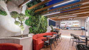 A modern bar area with a curved red sofa, black chairs, and a wooden ceiling with exposed beams. - Soho Boutique Equitativa (Málaga)