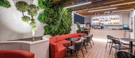 A modern bar area with a curved red sofa, black chairs, and a wooden ceiling with exposed beams.
