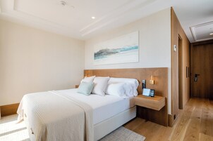 A modern hotel room with a large bed, a wooden headboard, a bedside table with a lamp, and a painting on the wall.