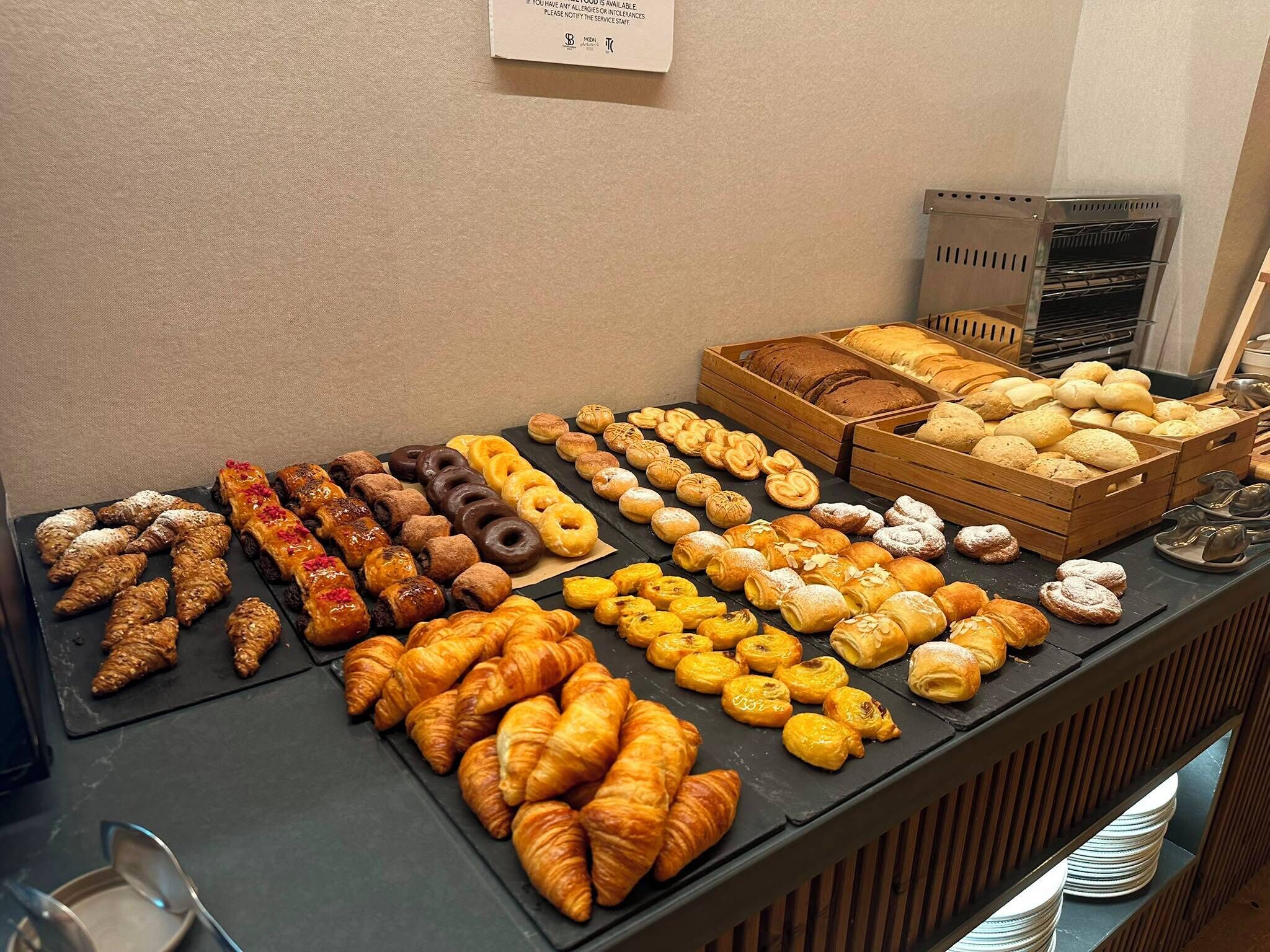 A buffet with various baked goods including pastries, bread, and rolls.
