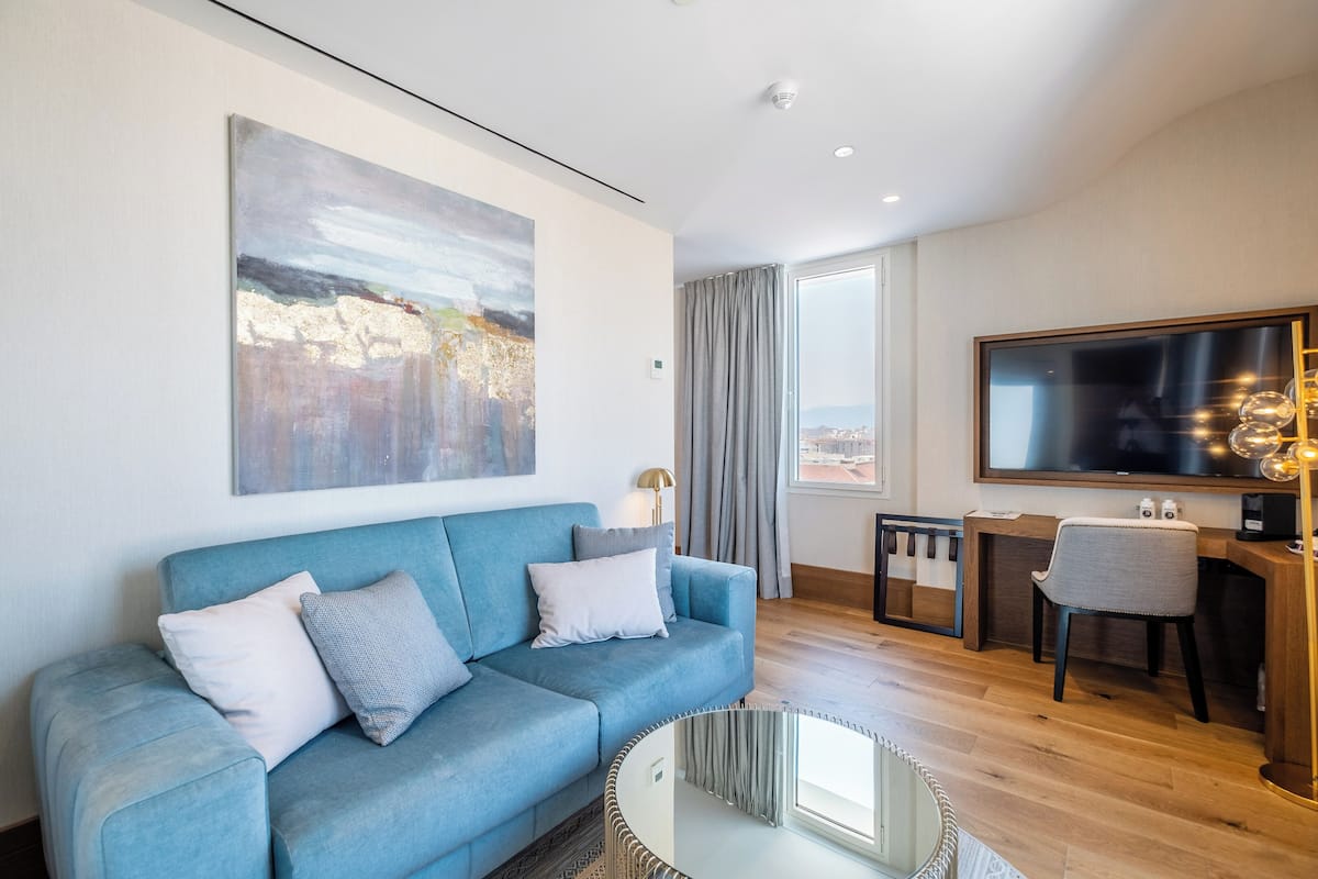 A modern living room with a blue sofa, a large abstract painting, a flat-screen TV, and a dining area with a table and chairs.