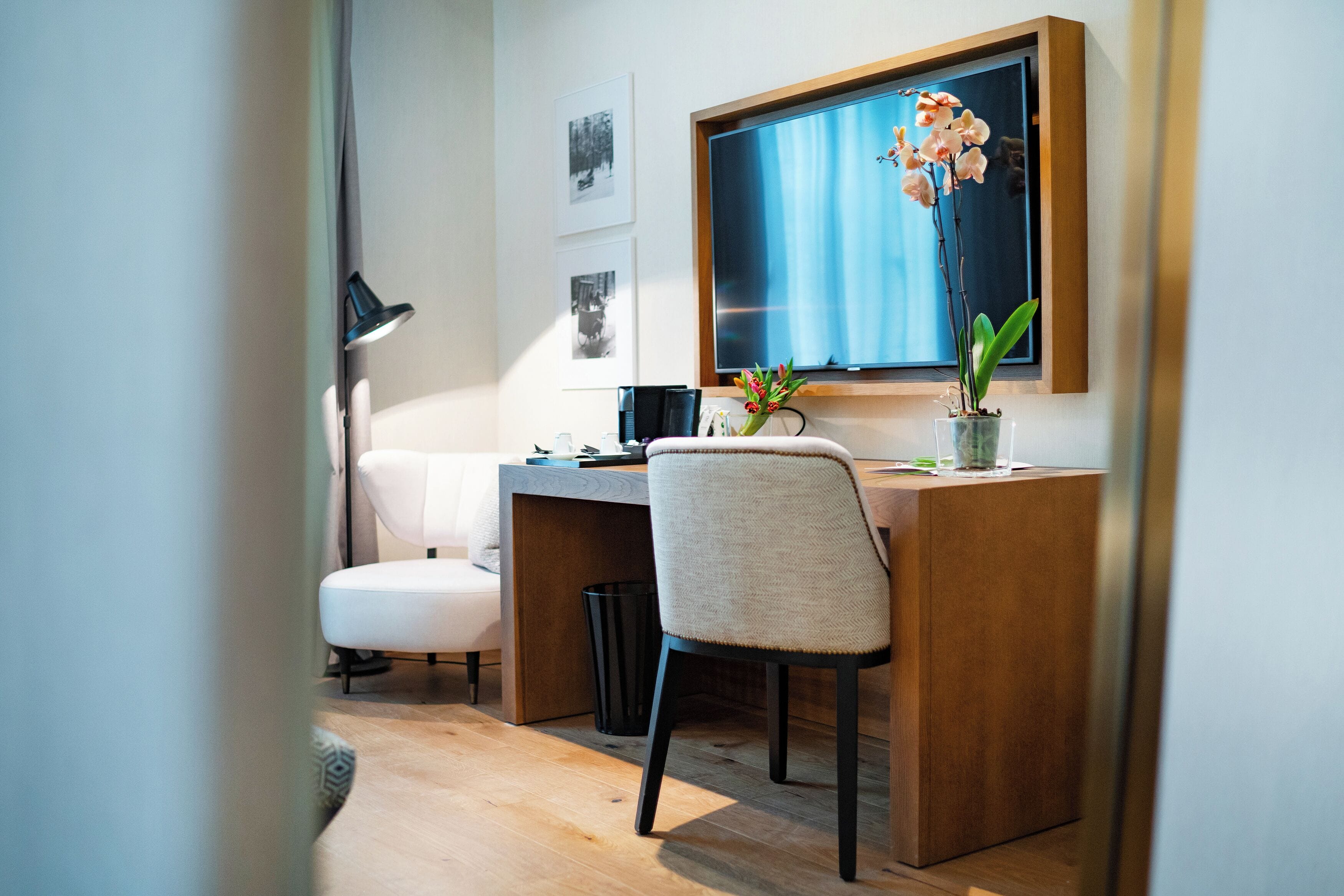 Un espacio de oficina moderno con un escritorio de madera, una silla blanca, un bote de basura negro y una orquídea en maceta.