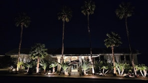 A well-lit building with a prominent entrance, surrounded by palm trees.