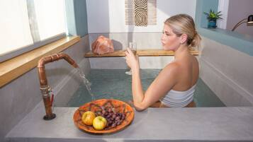 Una mujer en una bañera con un estante de madera, una gran roca y un cuenco de fruta.