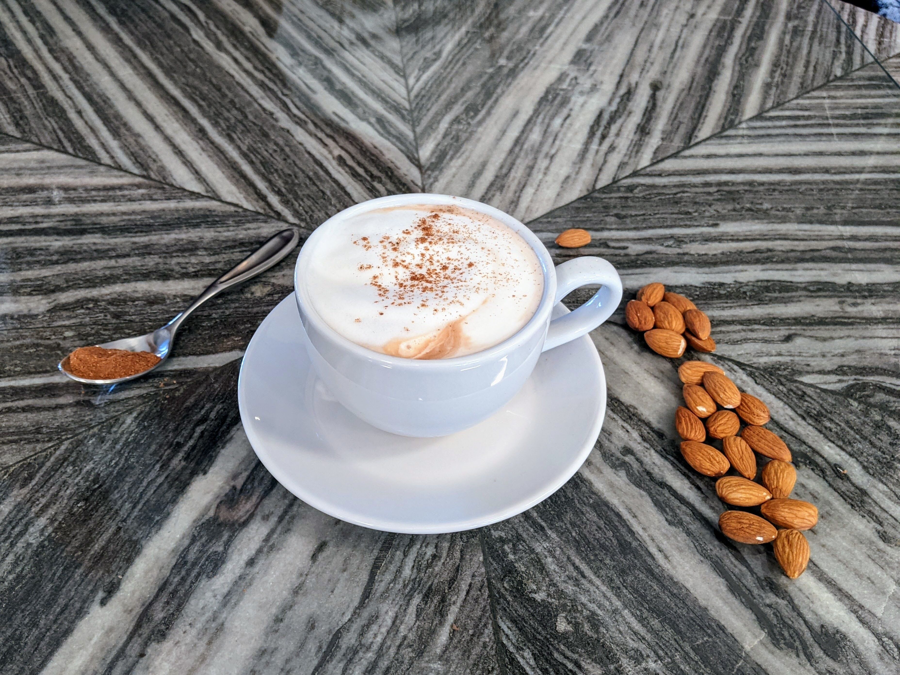 Eine weiße Kaffeetasse mit einem Löffel Zimt auf einem Marmortisch.