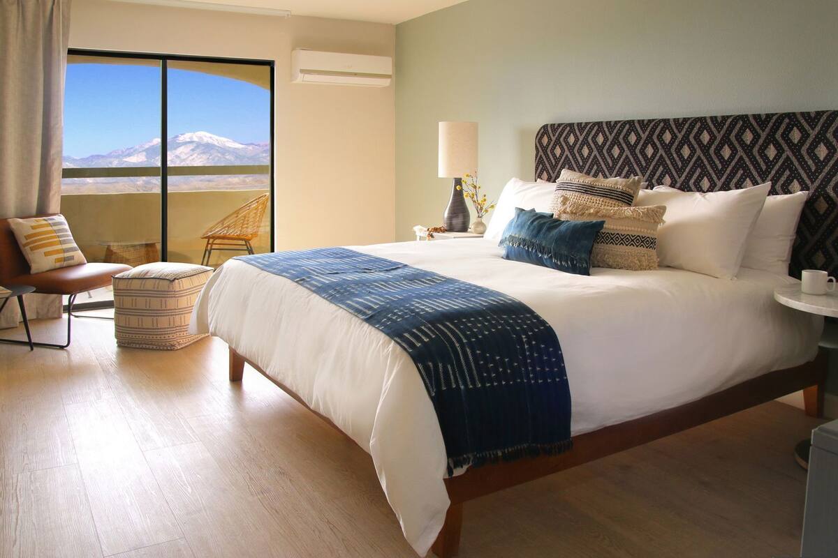 A hotel room with a large bed, a chair, a table, and a view of a mountain.