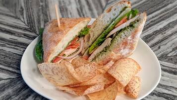 Un sándwich con lechuga, tomate y salsa verde, acompañado de papas fritas en un plato blanco.