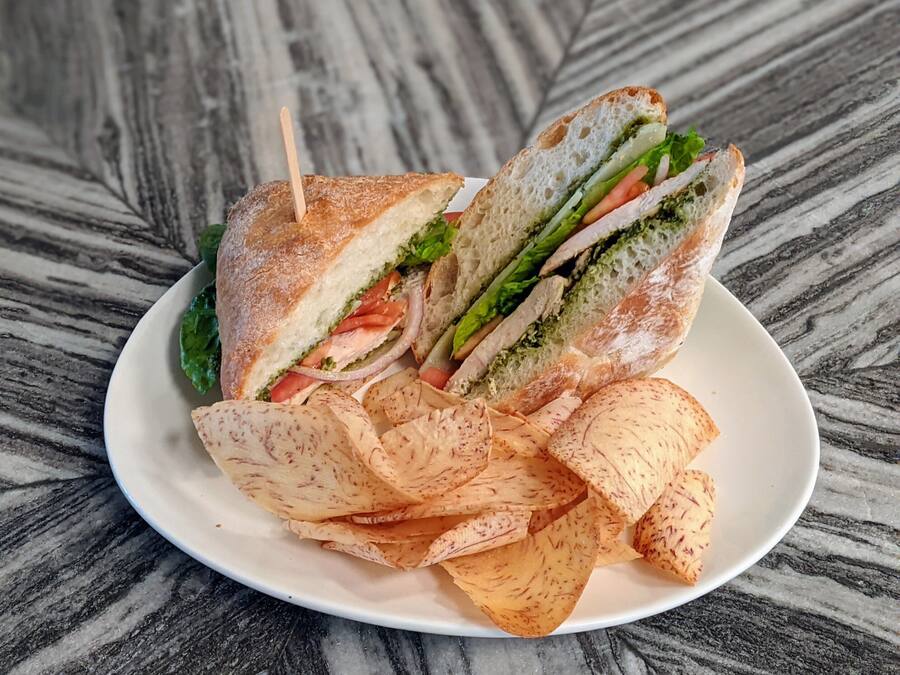 Un sándwich con lechuga, tomate y salsa verde, acompañado de papas fritas en un plato blanco.
