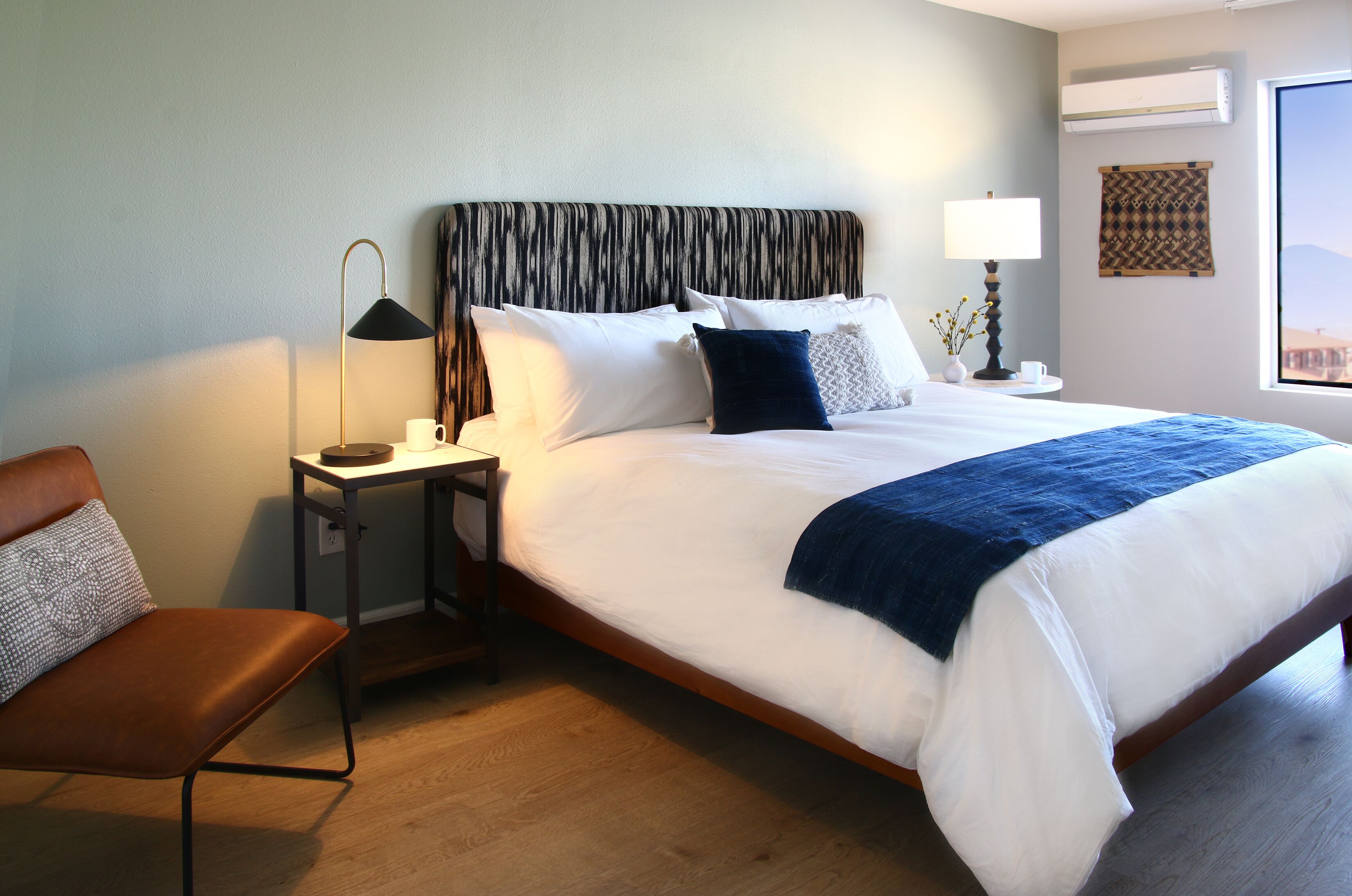 A hotel room with a large bed, a nightstand with a lamp, a chair, and a view of the outdoors.
