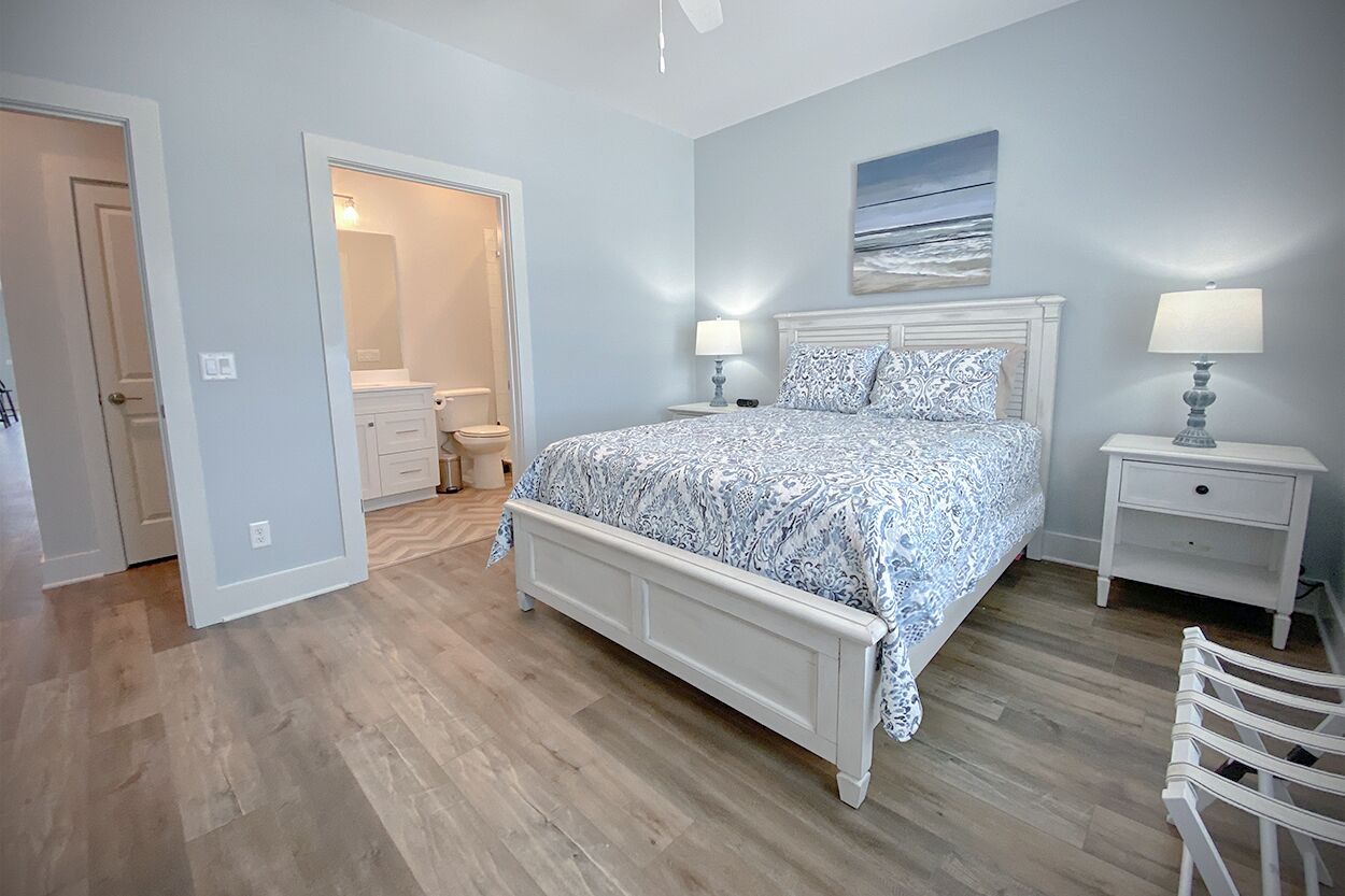 A bedroom with a bed, bedside tables, a nightstand, a chair, and a bathroom visible through an open door.
