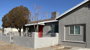 A residential house with a grey exterior, a red door, and a fenced yard.