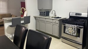 A compact kitchen with a microwave, sink, and stove. There is a dining area with chairs and a table.