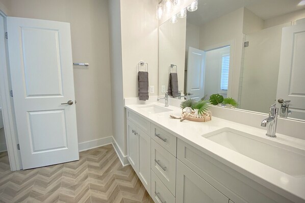 A modern bathroom with a large mirror, two sinks, and a herringbone-patterned floor.