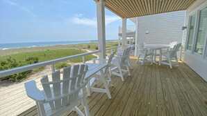 Um deck coberto com cadeiras brancas e uma mesa, com vista para uma praia e o oceano.