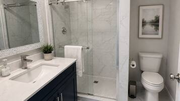 A bathroom with a shower, toilet, sink, and a framed picture on the wall.