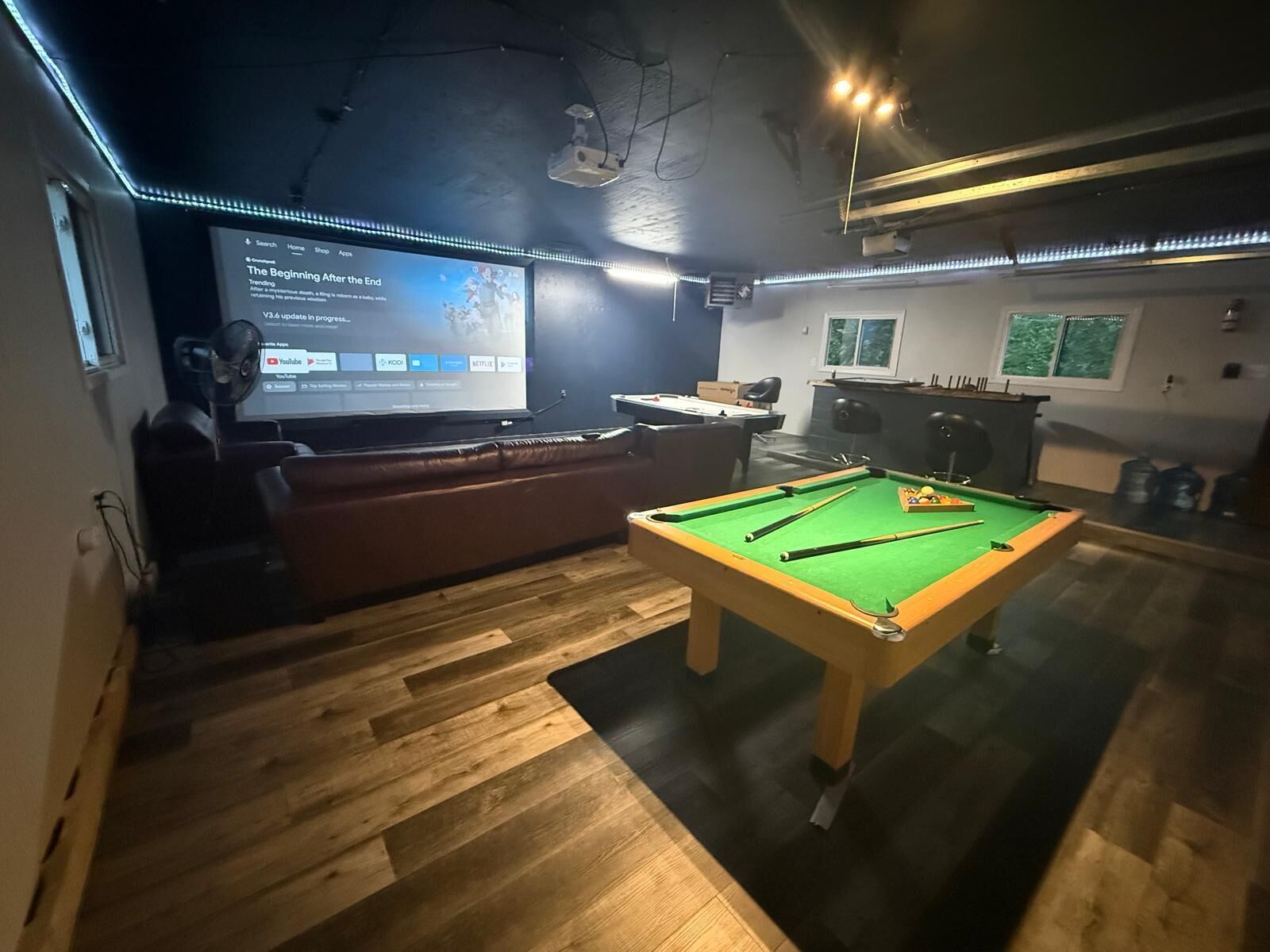 A room with a pool table, a projector screen displaying a movie, and a sofa.