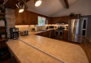 A modern kitchen with wooden cabinets, a stainless steel refrigerator, a built-in oven, a microwave, and a coffee maker.