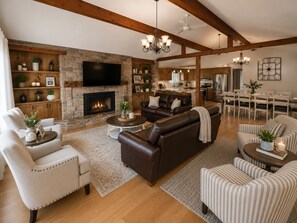 A spacious living room with a fireplace, leather sofas, a flat-screen TV, wooden beams, and a dining area.