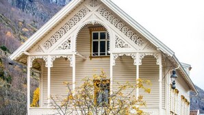 A white building with intricate lacework on the facade, a central arched window, and a balcony with a lamp post. - Lindstrøm Hotel (Laerdal)