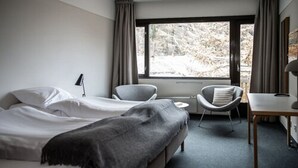 A modern hotel room with two beds, a desk, a chair, and a window with a view of trees. - Lindstrøm Hotel (Laerdal)
