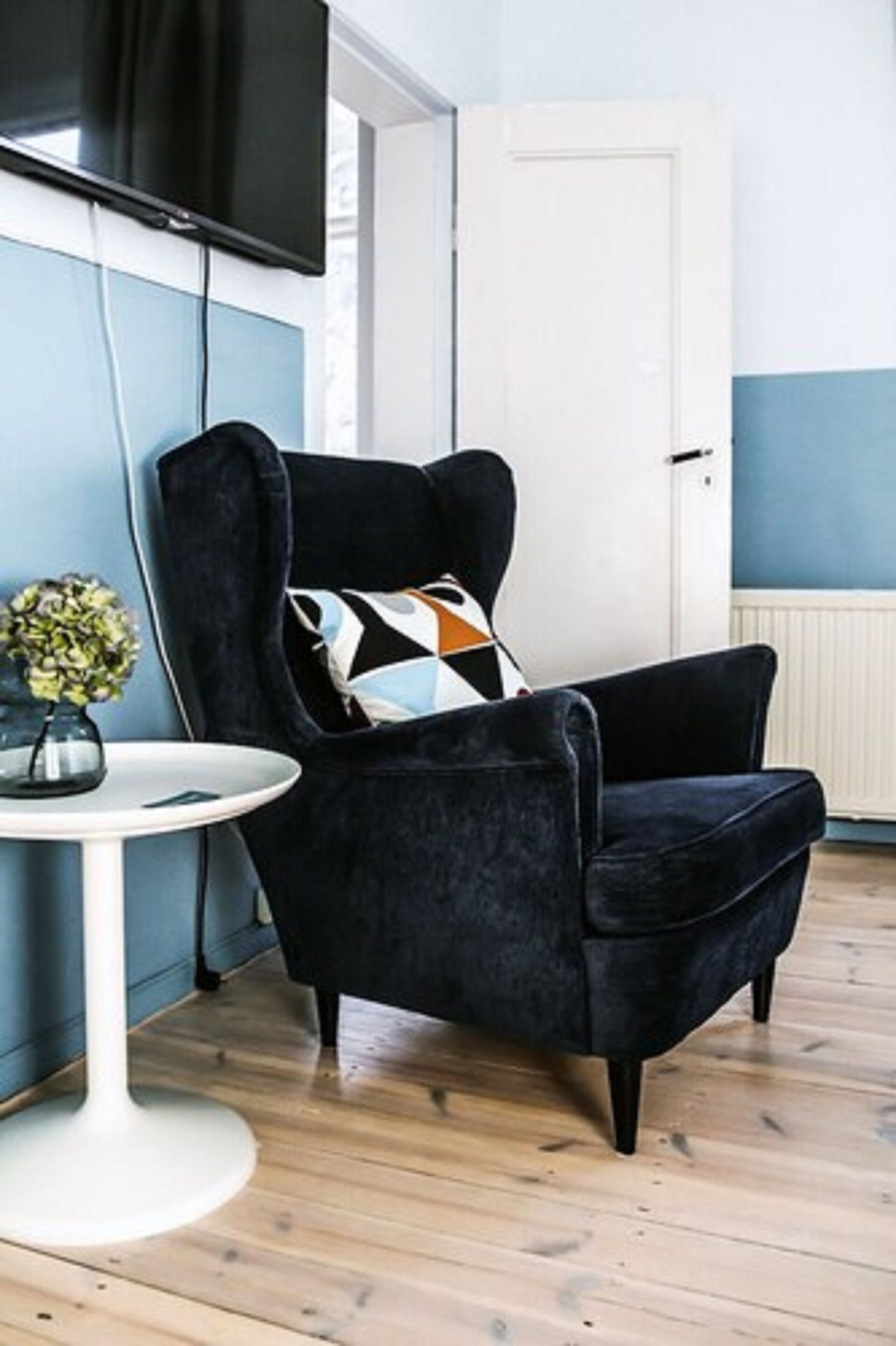 A modern living room with a dark velvet armchair, a round white side table, and a decorative pillow.