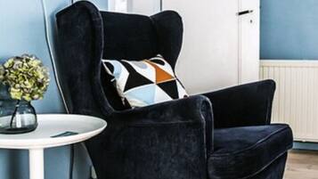 A modern living room with a dark velvet armchair, a round white side table, and a decorative pillow.