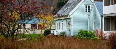 A light blue house with a gabled roof and a small porch, surrounded by autumn foliage and a hill in the background.