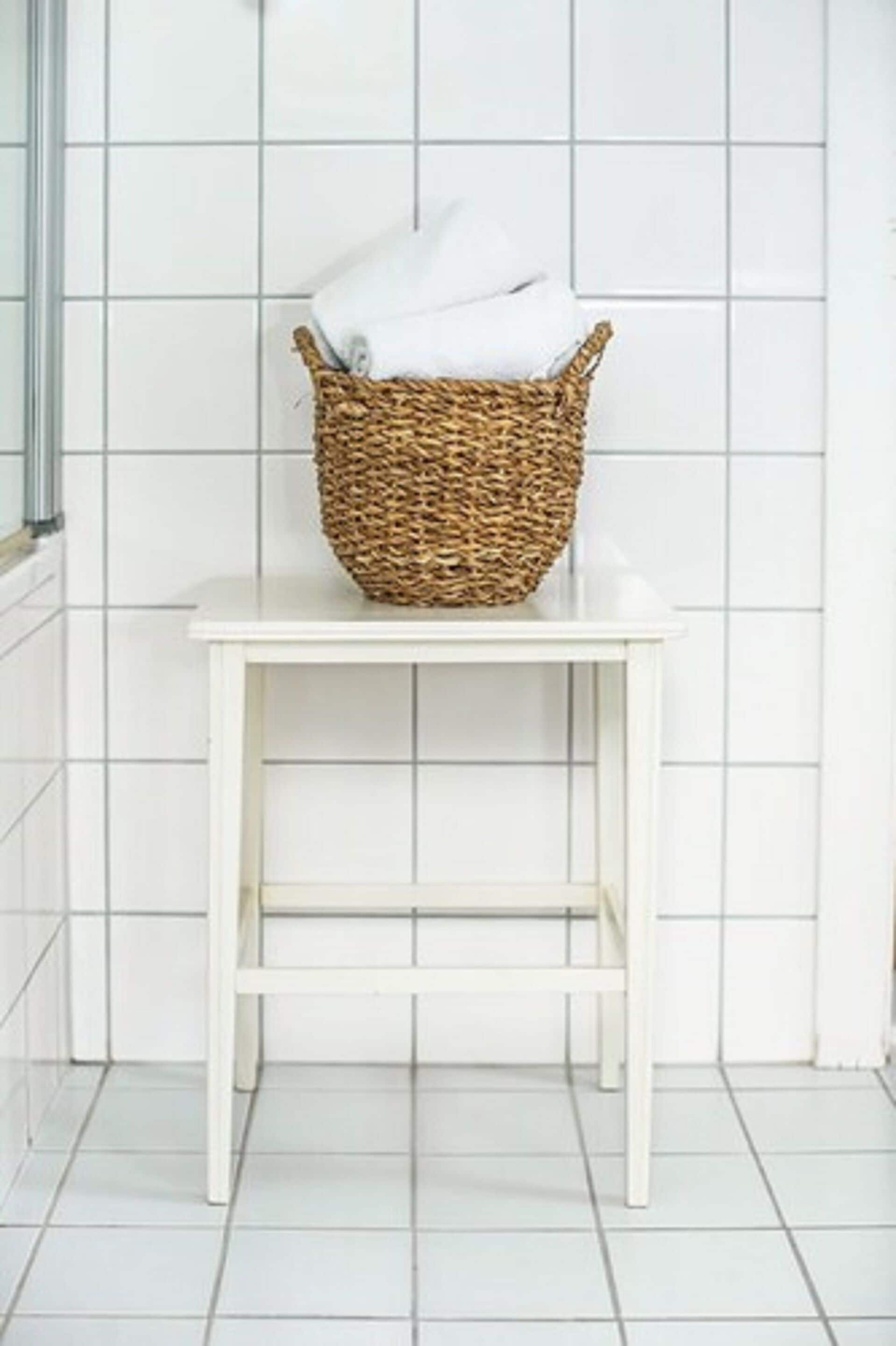 A white wicker basket on a white table against a white tiled wall.