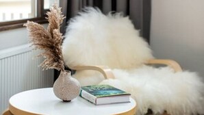 A cozy room with a round wooden table, a fluffy white chair, a small white vase with dried pampas grass, and a book. - Lindstrøm Hotel (Laerdal)