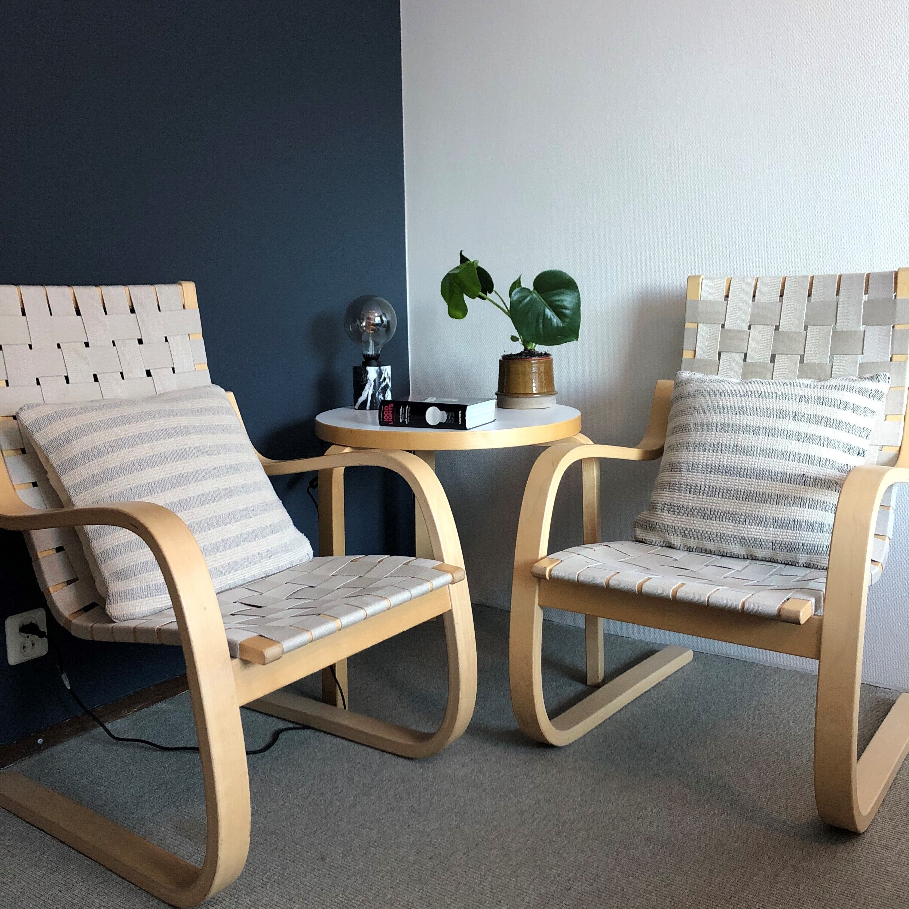 Two wooden rocking chairs with woven seats and backs, a small round table with a potted plant, and a power outlet on the floor.