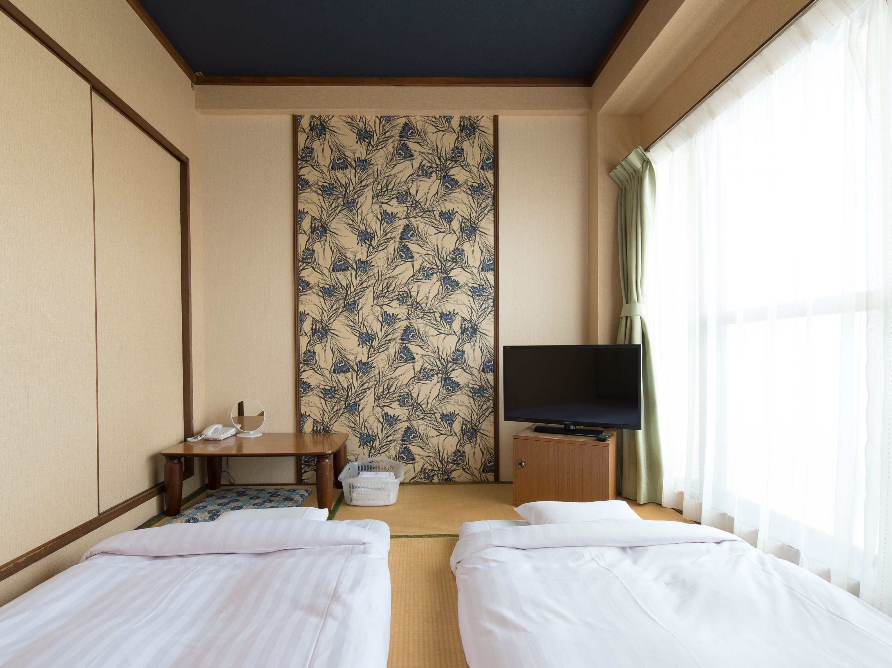A hotel room with two beds, a television, a small table with a phone and a basket, and a patterned wallpaper.