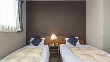 Een hotelkamer met twee enkele bedden, een nachtkastje met een lamp en een raam met gordijnen.