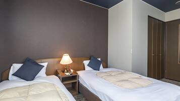 Hotellihuone, jossa on kaksi sänkyä, yöpöytä lampun kanssa ja vaatekaappi.