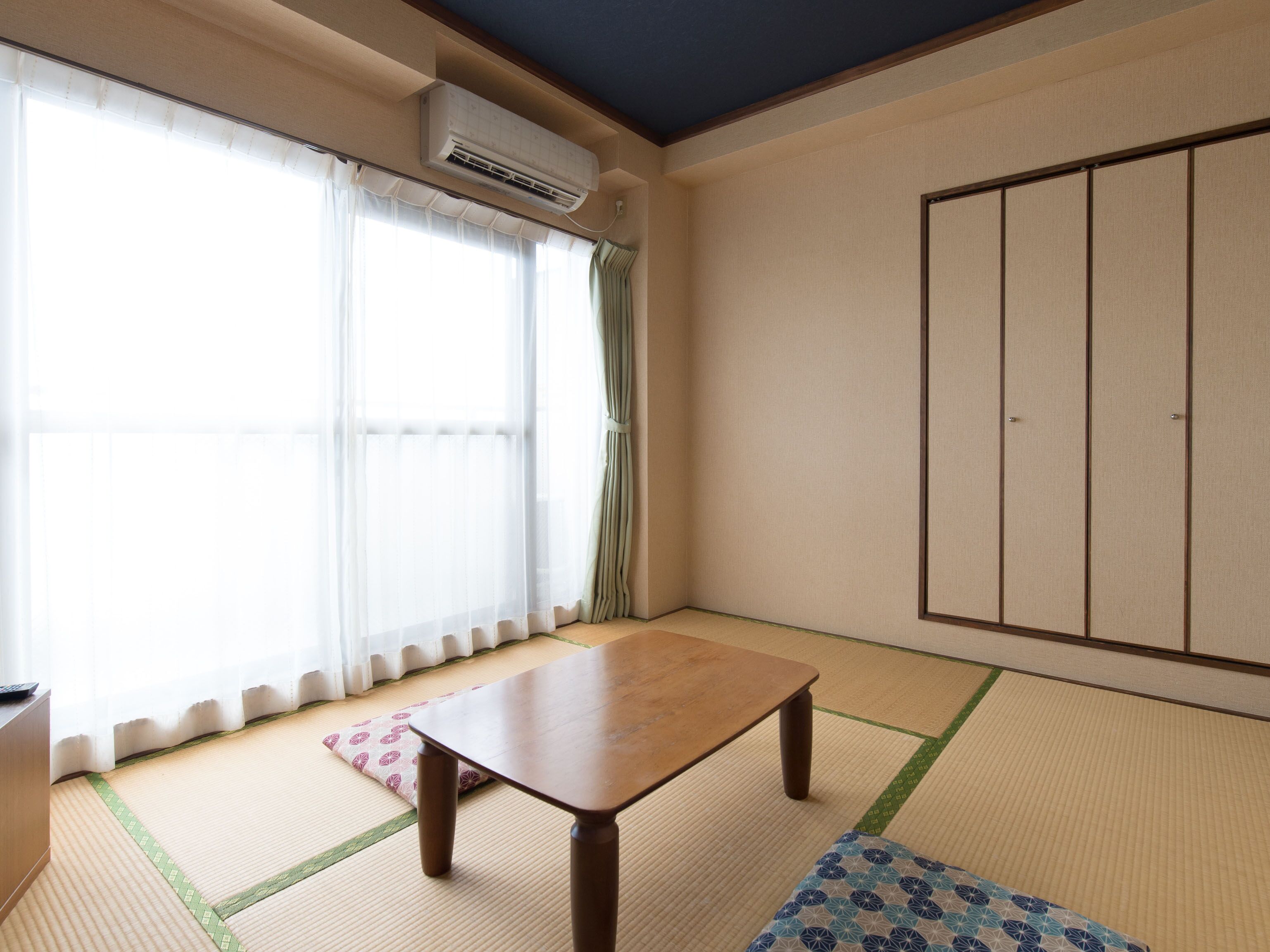 A room with tatami flooring, a wooden table, a wardrobe, and a sliding door with curtains.