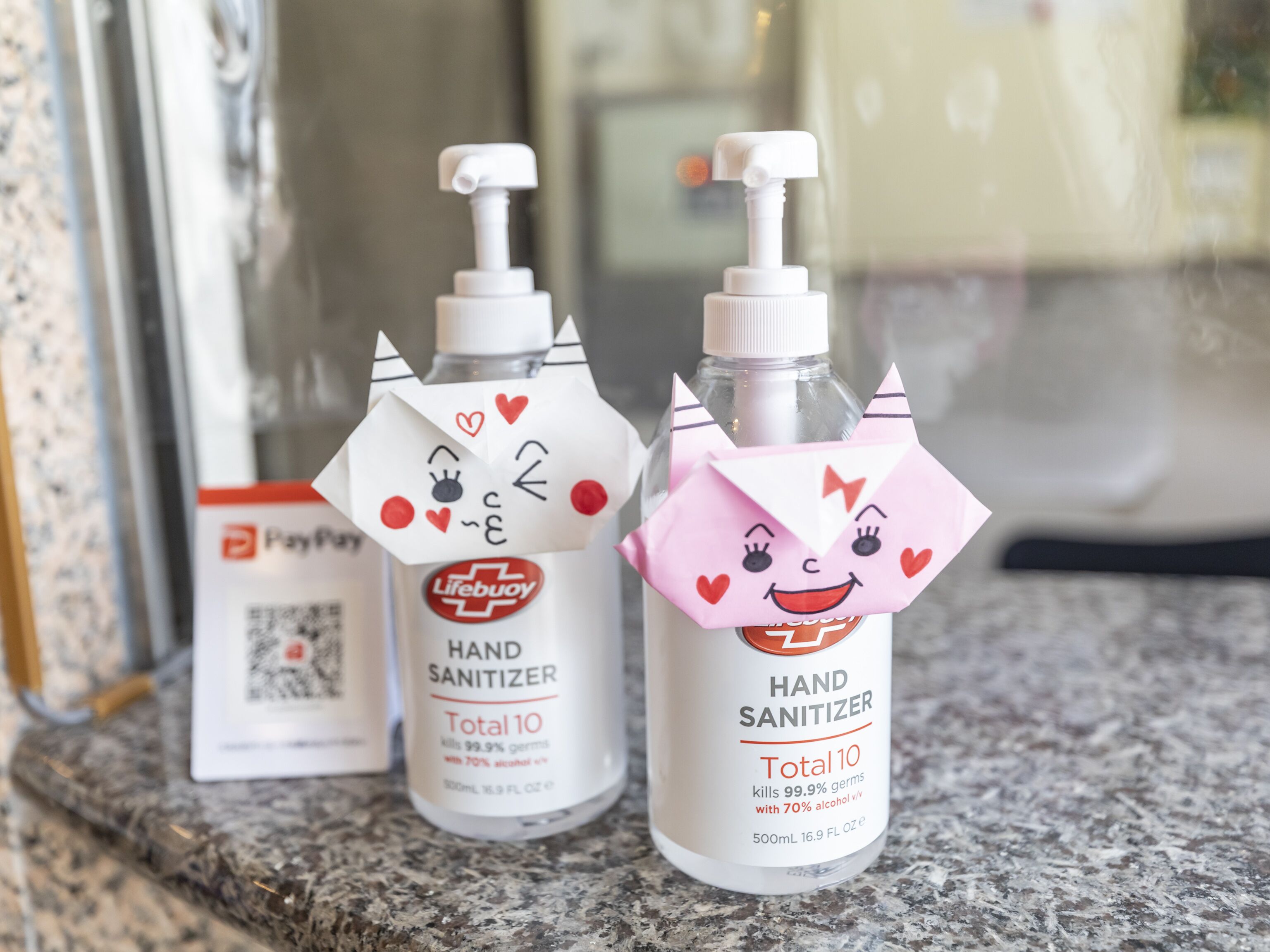 Twee desinfecterende handgel flessen met kattengezichtjes op een aanrecht.