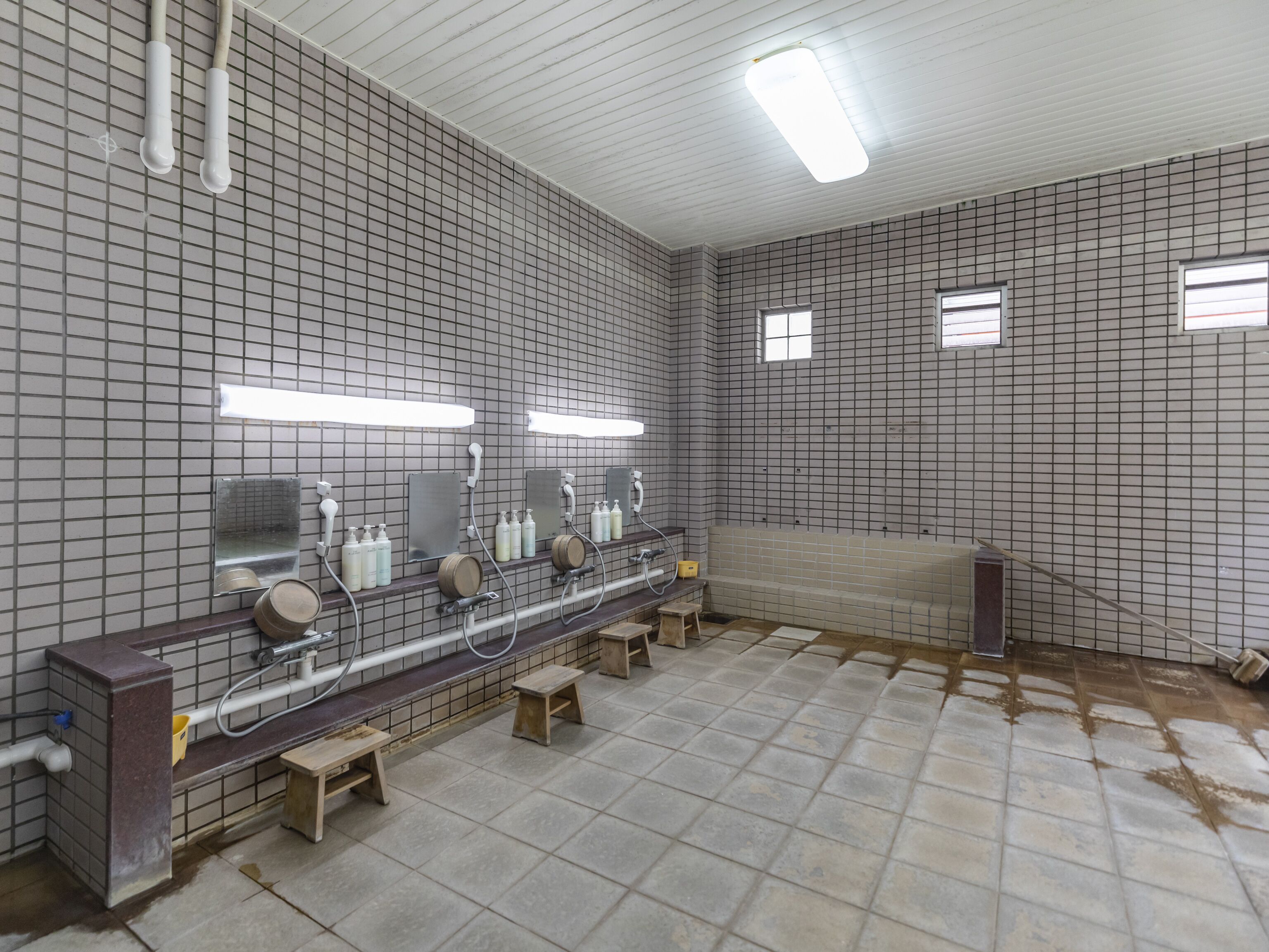A restroom with tiled walls, a long bench with sinks, and overhead lighting.