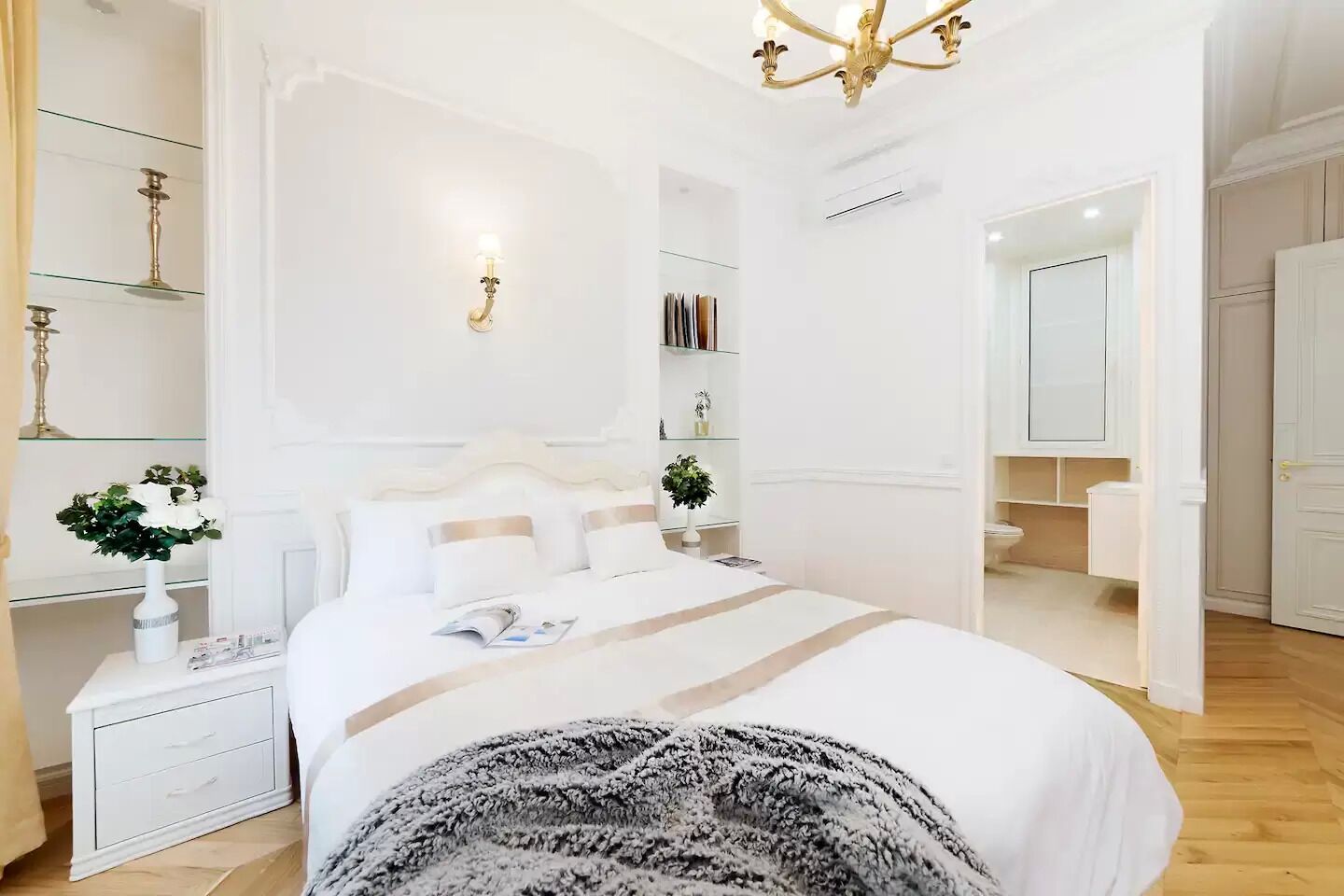 Une chambre moderne avec un grand lit, des tables de chevet, un lustre et une bibliothèque.