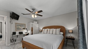 Ein Schlafzimmer mit einem großen Bett, einem Deckenventilator, einem an der Wand montierten Fernseher und einem Schreibtisch mit einem Computer.