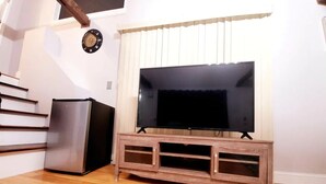 Un saló amb un moble de televisió de fusta, un televisor de pantalla plana, un frigorífic d'acer inoxidable i una escala.