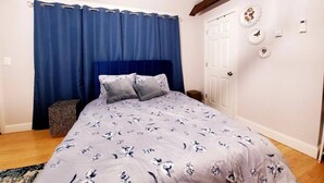 Un dormitori amb un llit, cortines blaves, una porta blanca i decoracions a la paret.
